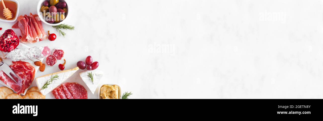 Assortimento di formaggi e antipasti di carne. Vista dall'alto bordo d'angolo su sfondo di banner in marmo bianco con spazio per la copia. Foto Stock
