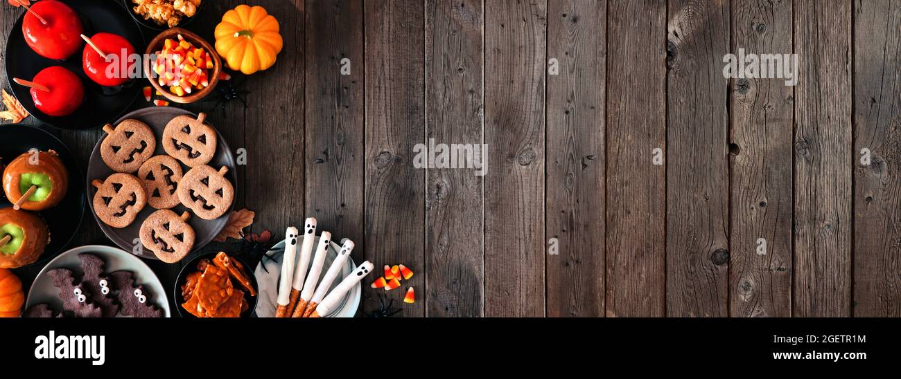 Rustico Halloween trattare angolo bordo su uno sfondo di legno scuro banner con spazio copia. Vista dall'alto. Assortimento di mele candite, biscotti, caramelle e sw Foto Stock