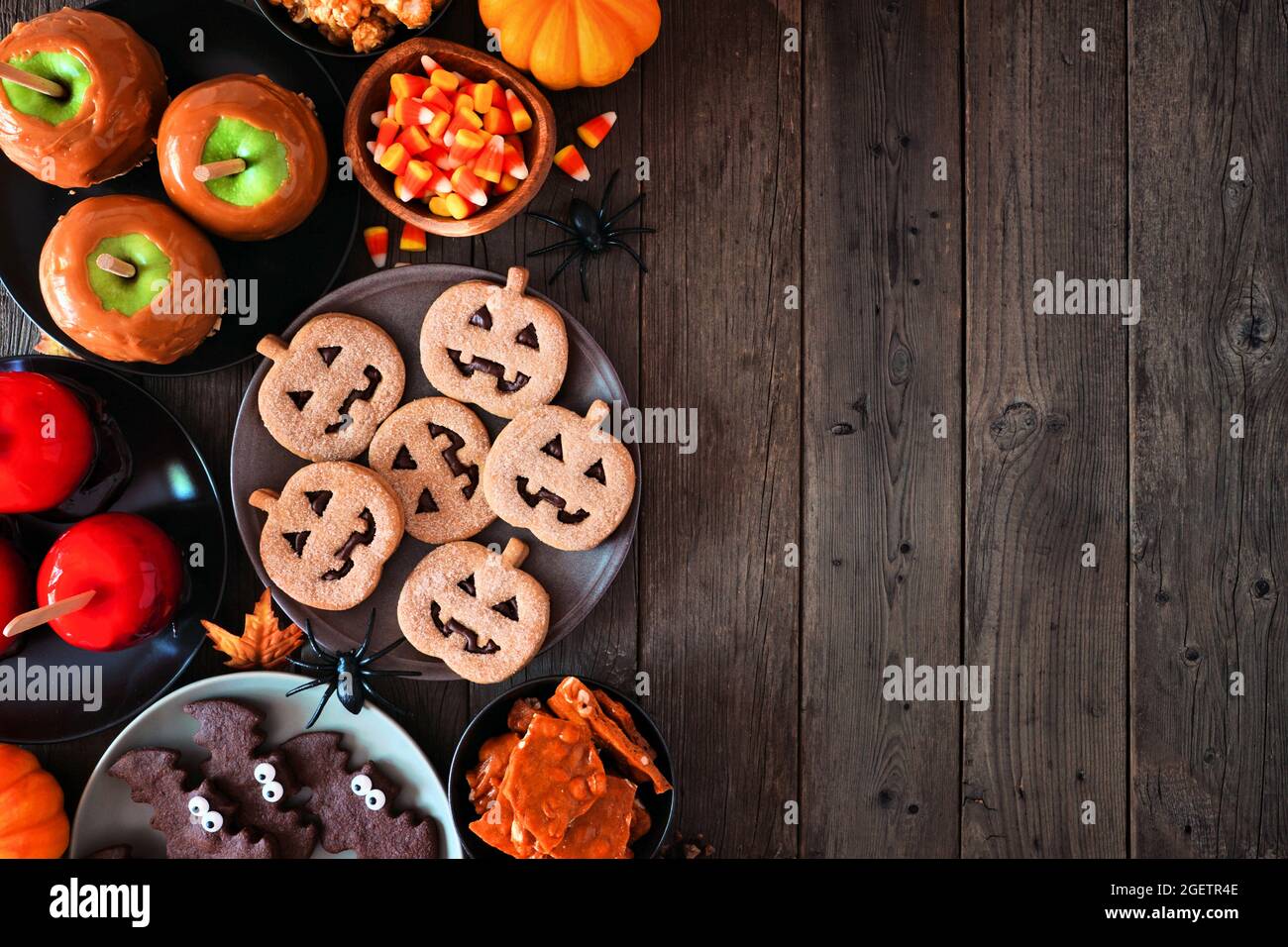 Halloween rustico trattare bordo laterale su uno sfondo di legno scuro con spazio copia. Vista dall'alto. Varietà di mele candite, biscotti, caramelle e dolci. Foto Stock