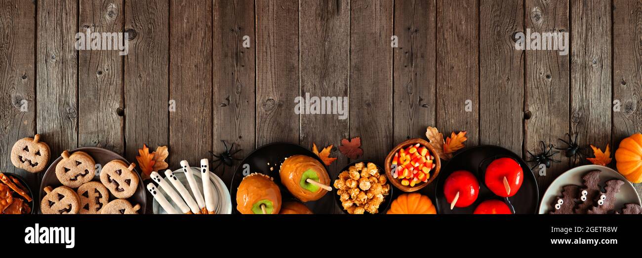 Halloween rustico trattare il bordo inferiore su uno sfondo di legno scuro banner con spazio copia. Vista dall'alto. Varietà di mele candite, biscotti, caramelle e swe Foto Stock