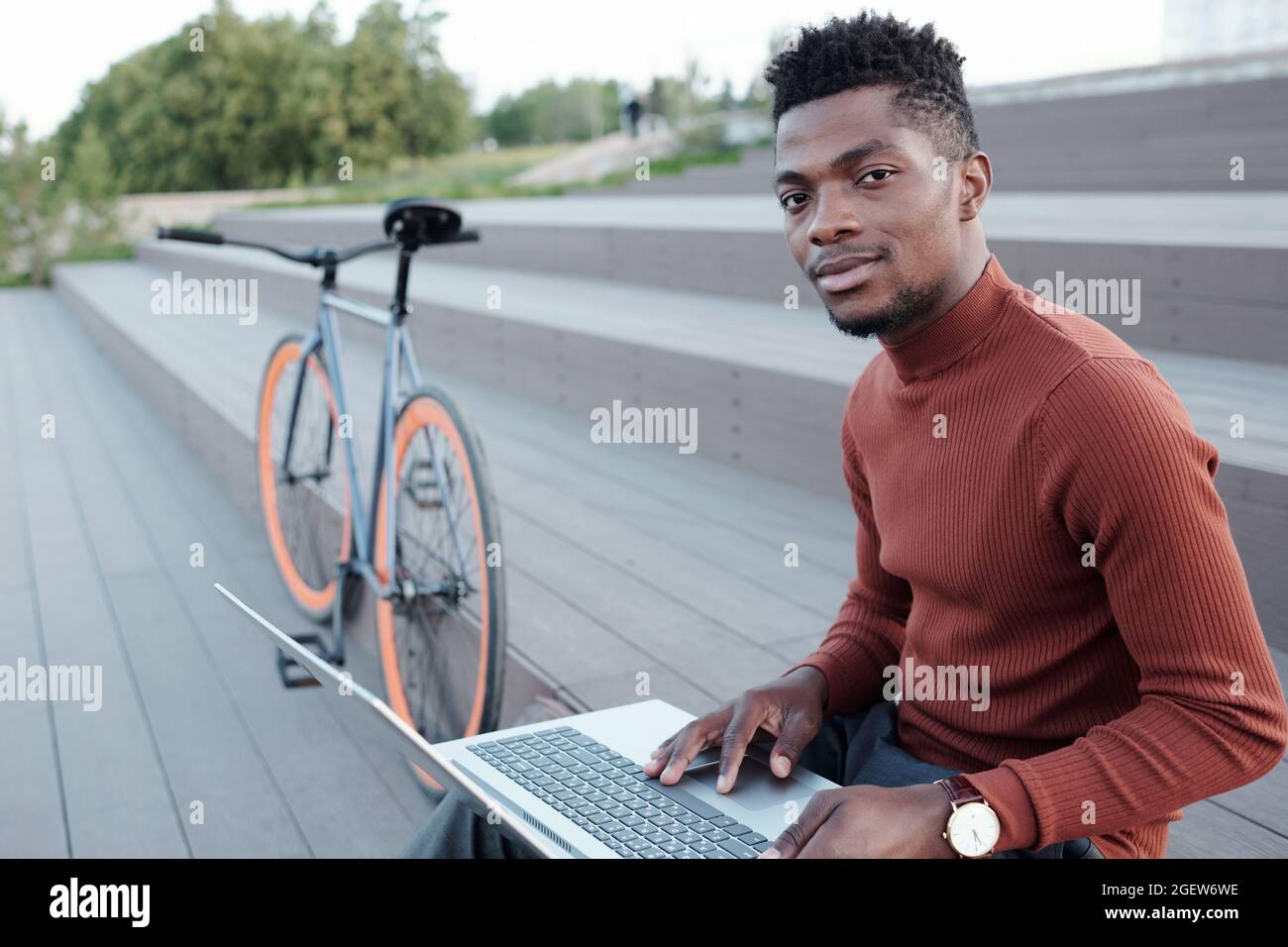 Giovane lavoratore contemporaneo con colletto bianco che utilizza un computer portatile in ambiente urbano Foto Stock