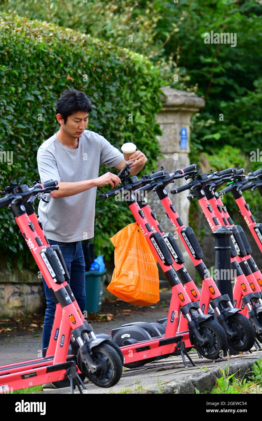 Una fila di voi-e-Scooters visto pronto per la gente a noleggio da cellulare che è fissato al centro del manubrio. Classificato come un veicolo stradale Foto Stock