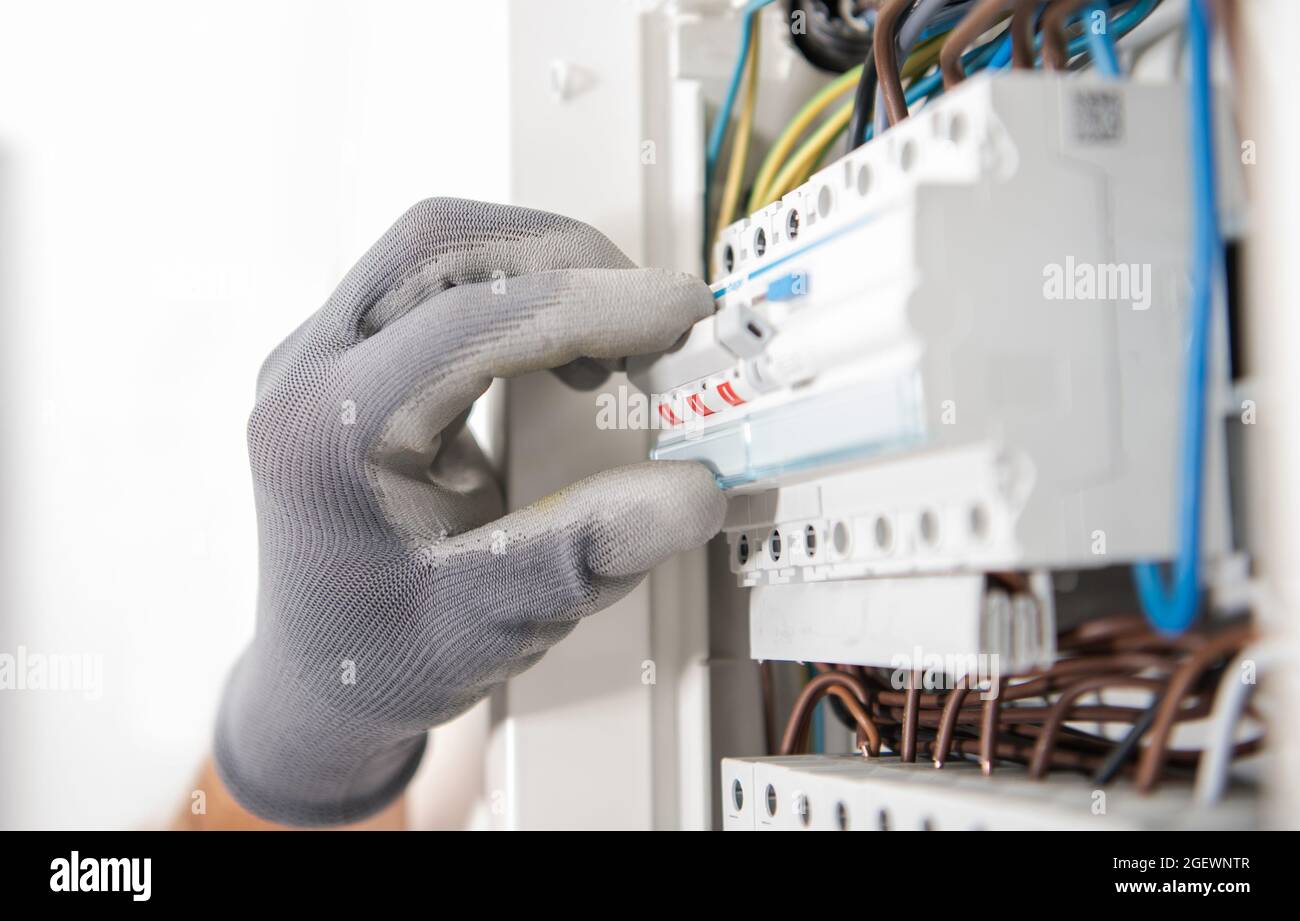 Elettricista che indossa guanti di sicurezza prova Fusibili all'interno di un appartamento situato cassetta elettrica. Foto Stock