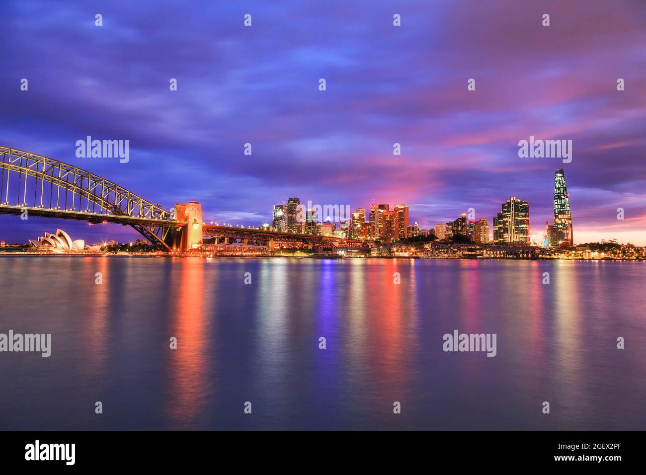Tramonto colorato sopra lo skyline del CBD di Sydney attraverso il porto di Sydney - le rocce, il Ponte del Porto, Barangaroo - luminoso. Foto Stock