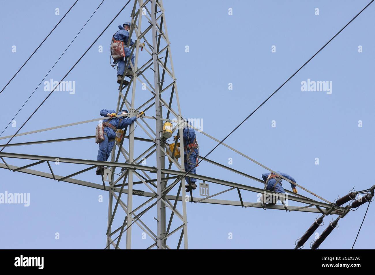 I climber industriali montano corde con casco e indumenti protettivi è fissato con una corda cancellato un palo di potenza di colore grigio. Foto Stock