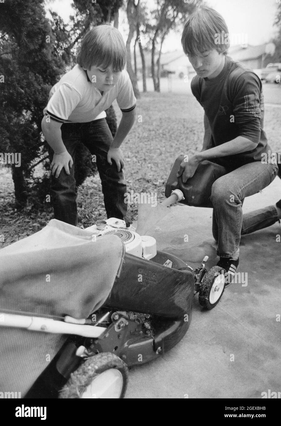 Austin Texas USA, circa 1990: Il ragazzo teen riempie il tosaerba di gas mentre lui e il suo fratello più giovane lavorano in estate tagliando i prati per i vicini. ©Bob Daemmrich Foto Stock