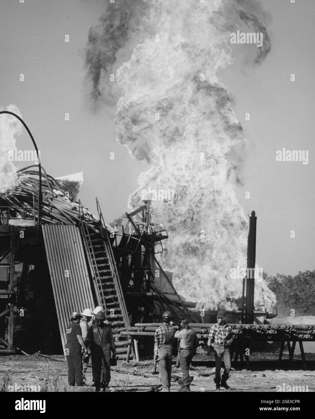 Giddings, Texas USA, circa 1986: Vigili del fuoco e lavoratori del carro di perforazione si trovano vicino al fuoco del pozzo petrolifero. ©Bob Daemmrich Foto Stock