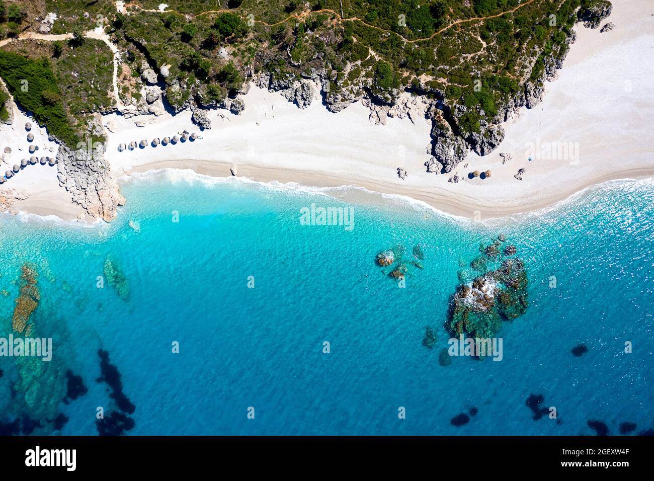 Vista aerea di file di lettini con ombrelloni di paglia sulla spiaggia. Paradiso sulla spiaggia e mare turchese preso dal drone, Albania, Europa Foto Stock