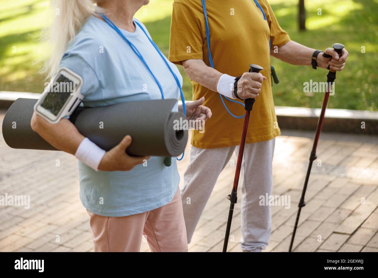Un paio di persone anziane con diverse attrezzature sportive camminano lungo la città verde Foto Stock