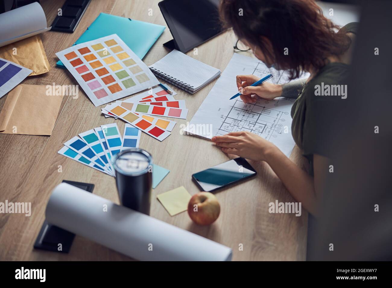 Primo piano del processo di lavoro del progettista di interni che fa le note su un blueprint, selezionando i campioni di colore, seduto al tavolo nel suo ufficio Foto Stock