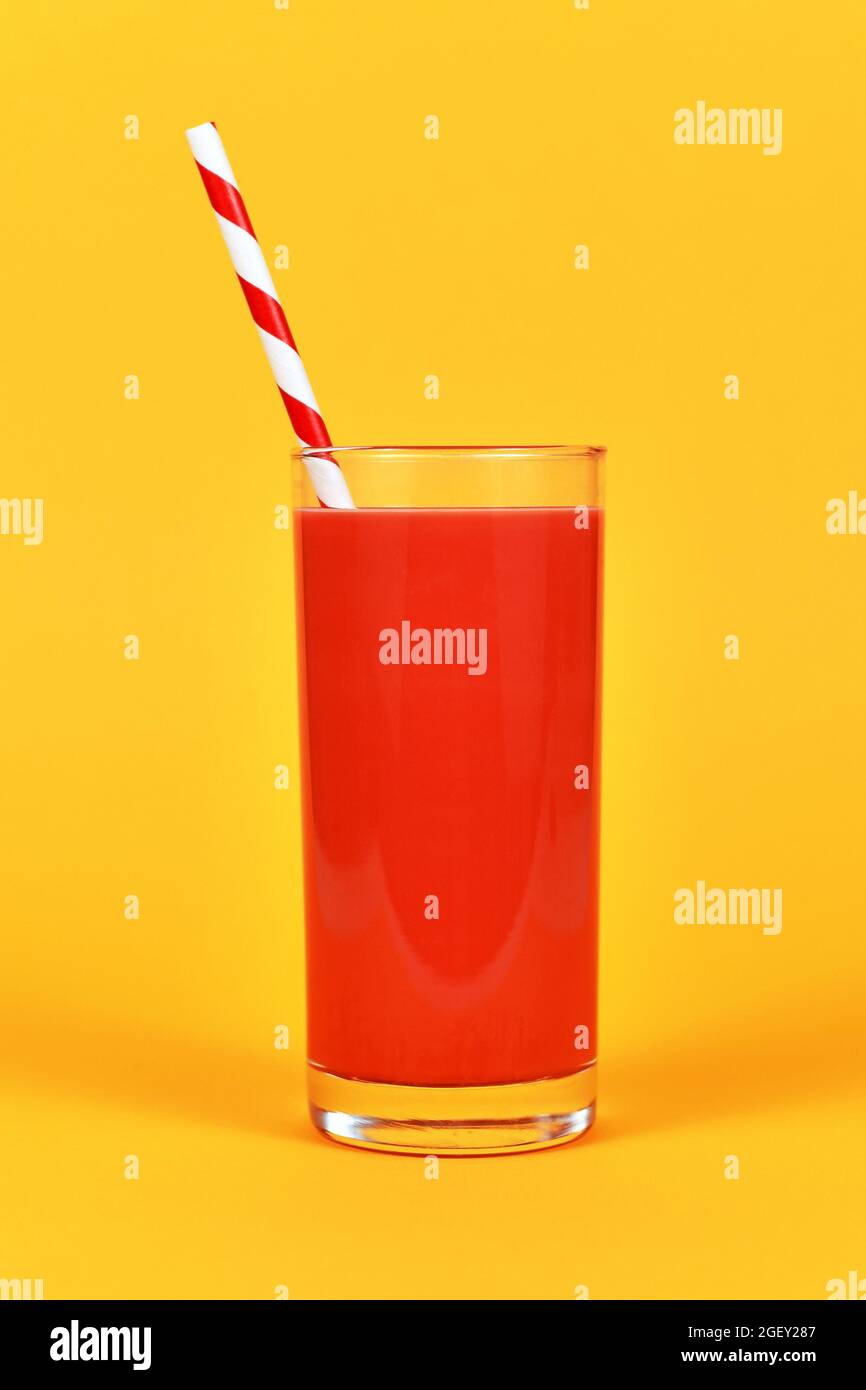 Bicchiere pieno con succo rosso e cannuccia a strisce davanti allo sfondo giallo Foto Stock