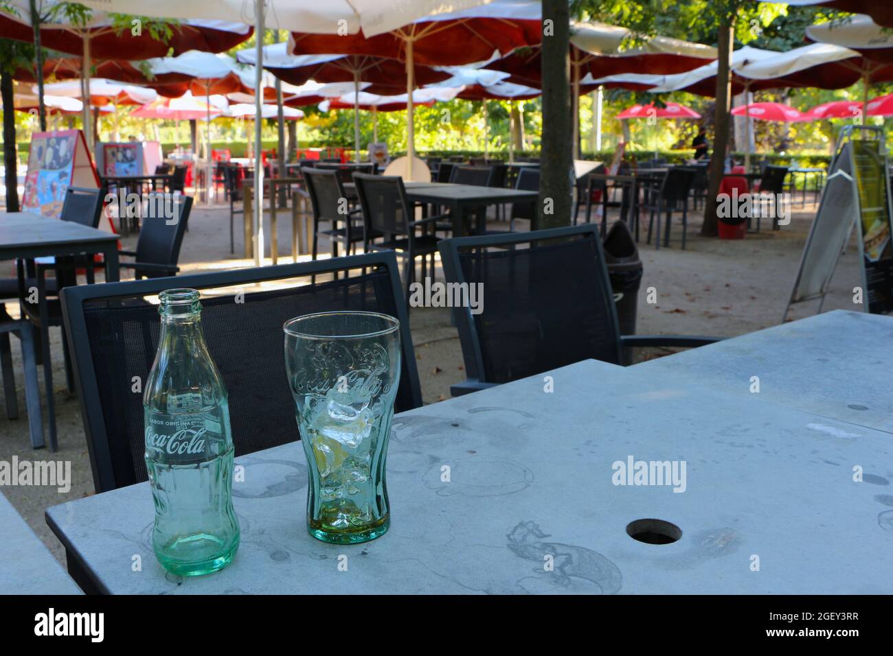 Bicchiere vuoto bottiglia Coca-Cola e bicchiere vuoto con ghiaccio e limone su un tavolo vuoto bar terrazza El Retiro parco Madrid Spagna Foto Stock