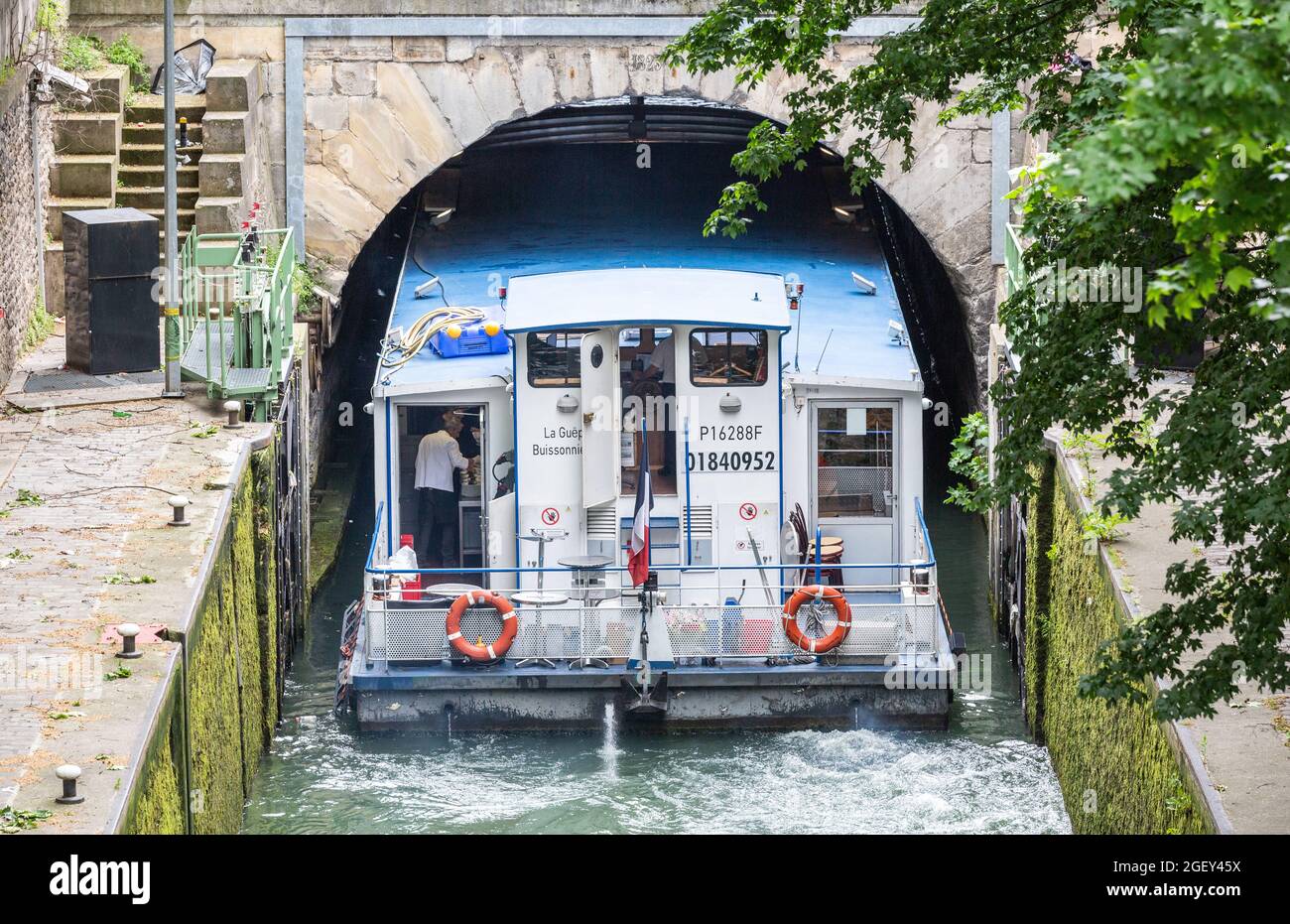 Barca turistica che entra sotto un ponte stretto del canale Saint-Martin a Parigi Foto Stock