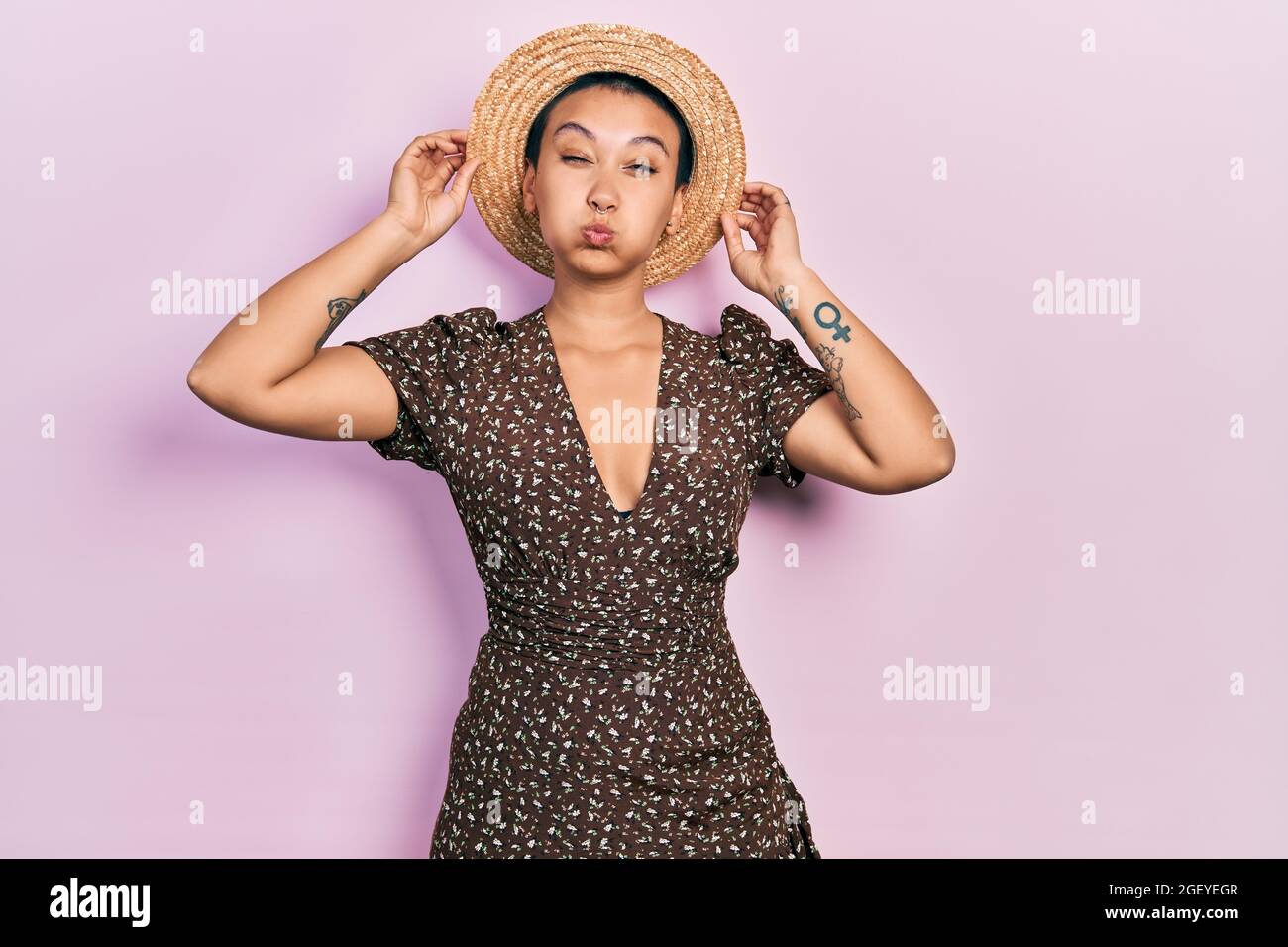 Bella donna ispanica con capelli corti indossando cappello estate puffing  guance con faccia divertente. Bocca gonfia di aria, cattura aria Foto stock  - Alamy