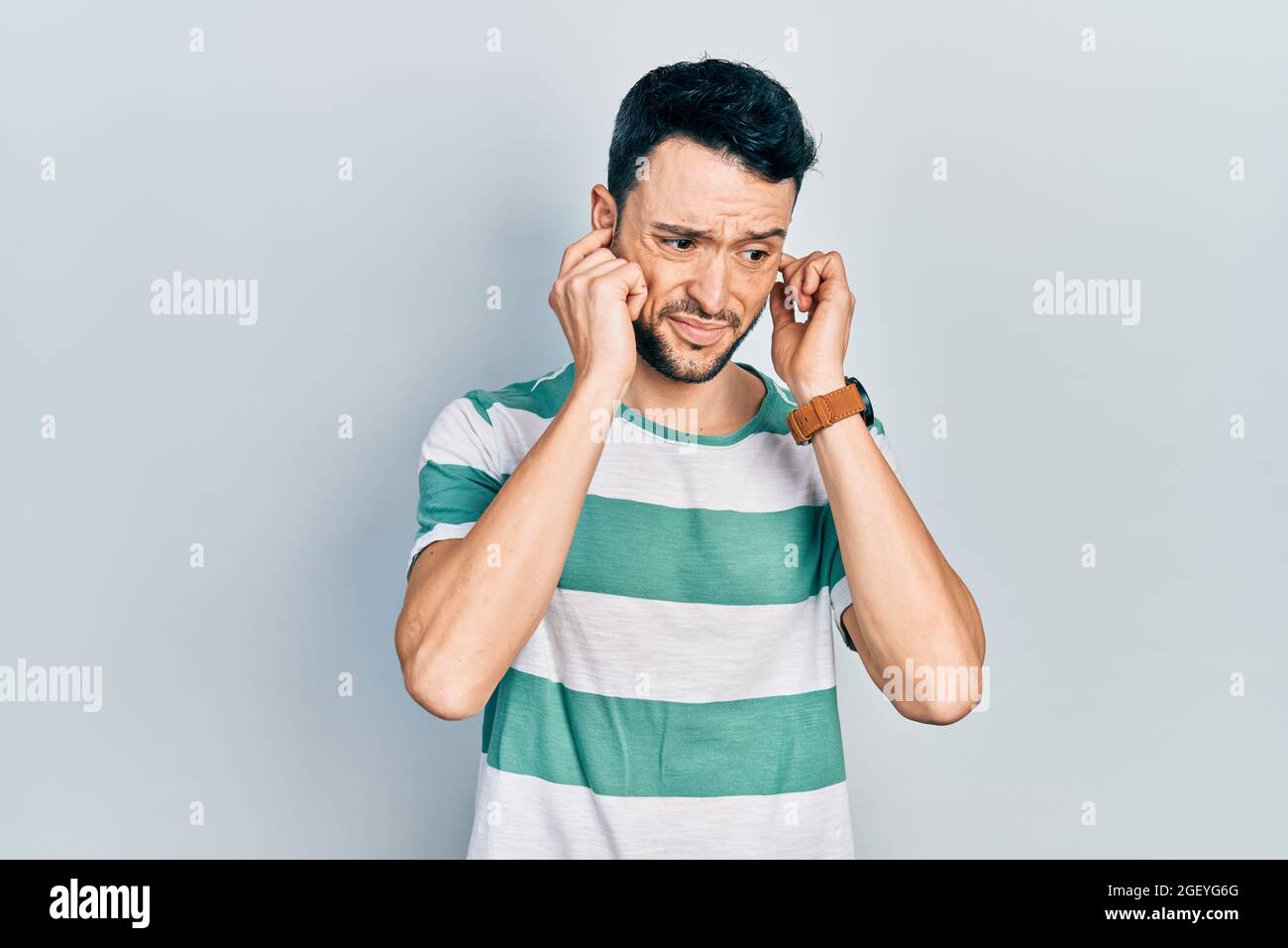 Giovane uomo ispanico che indossa abiti casual che coprono le orecchie con le dita con un'espressione seccata per il rumore della musica forte. Concetto sordomuti. Foto Stock