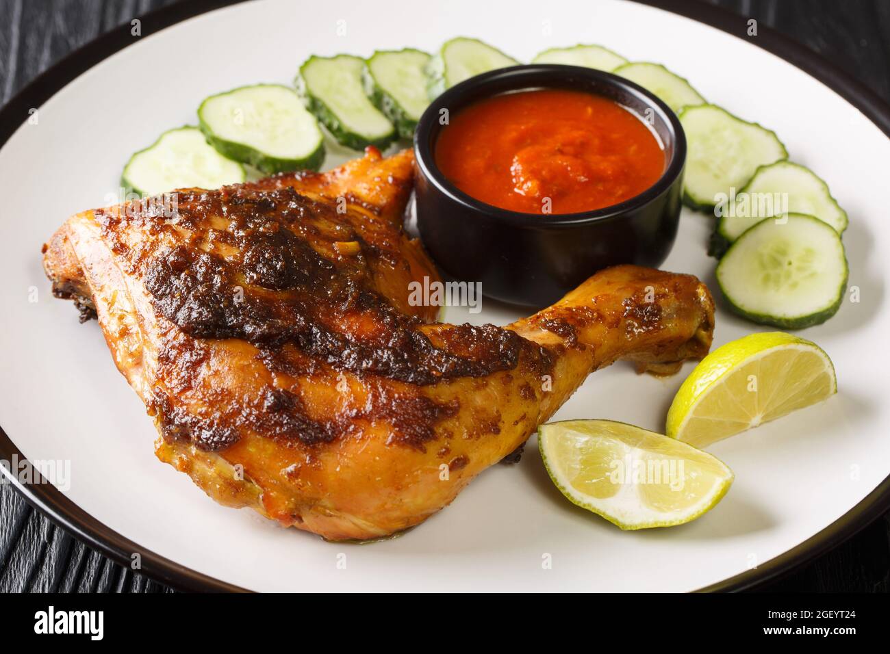 L'Ayam bakar è un piatto indonesiano e malese, composto da pollo grigliato al carbone servito con cetriolo e salsa calda a spicchio nel piatto sul Foto Stock