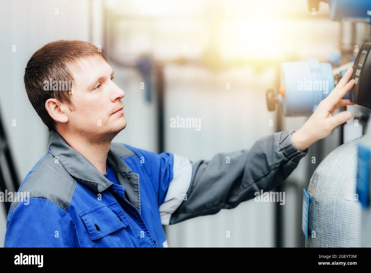 Un uomo in abiti da lavoro controlla i sensori della caldaia o della stazione di compressione. Monitoraggio del sistema. Progettazione al lavoro in un impianto industriale al chiuso. Una scena reale mentre si lavora. Foto Stock