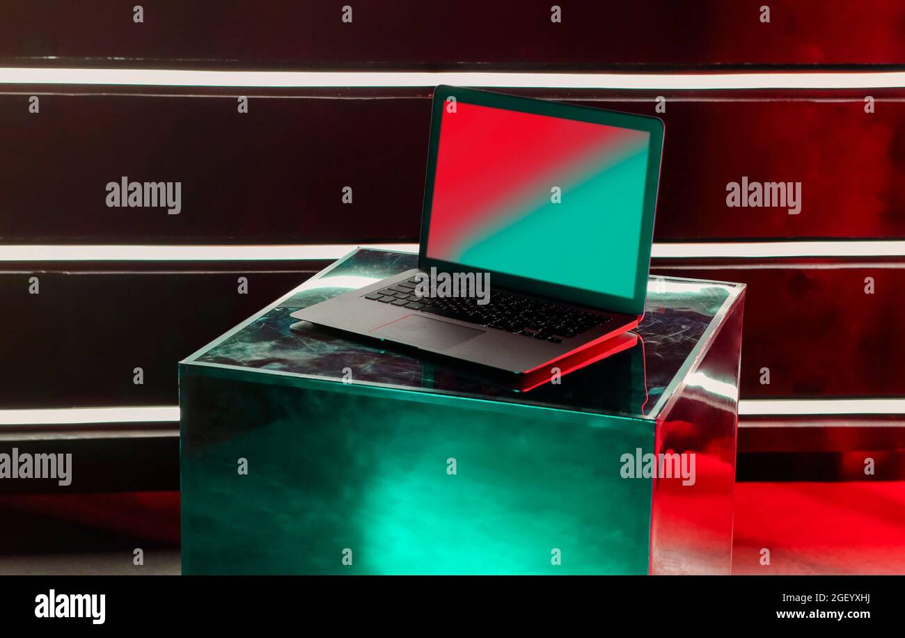 Computer laptop moderno aperto su un cubo lucido metallizzato di designer creativo con riflessi di raggi al neon sulla superficie del notebook con schermo bianco mock up, co Foto Stock