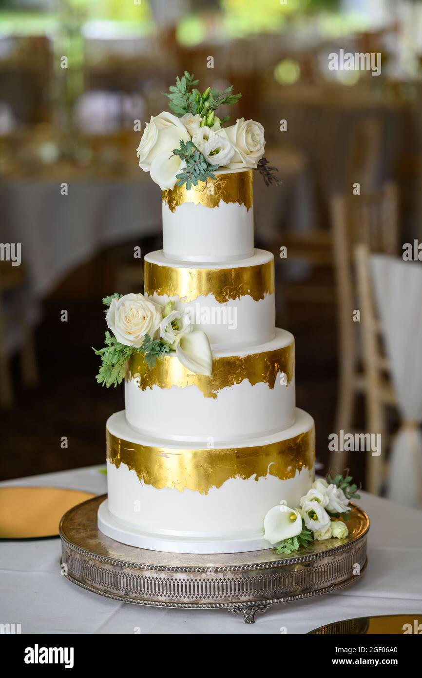 Torta nuziale a quattro piani con foglia d'oro e fiori freschi Foto Stock