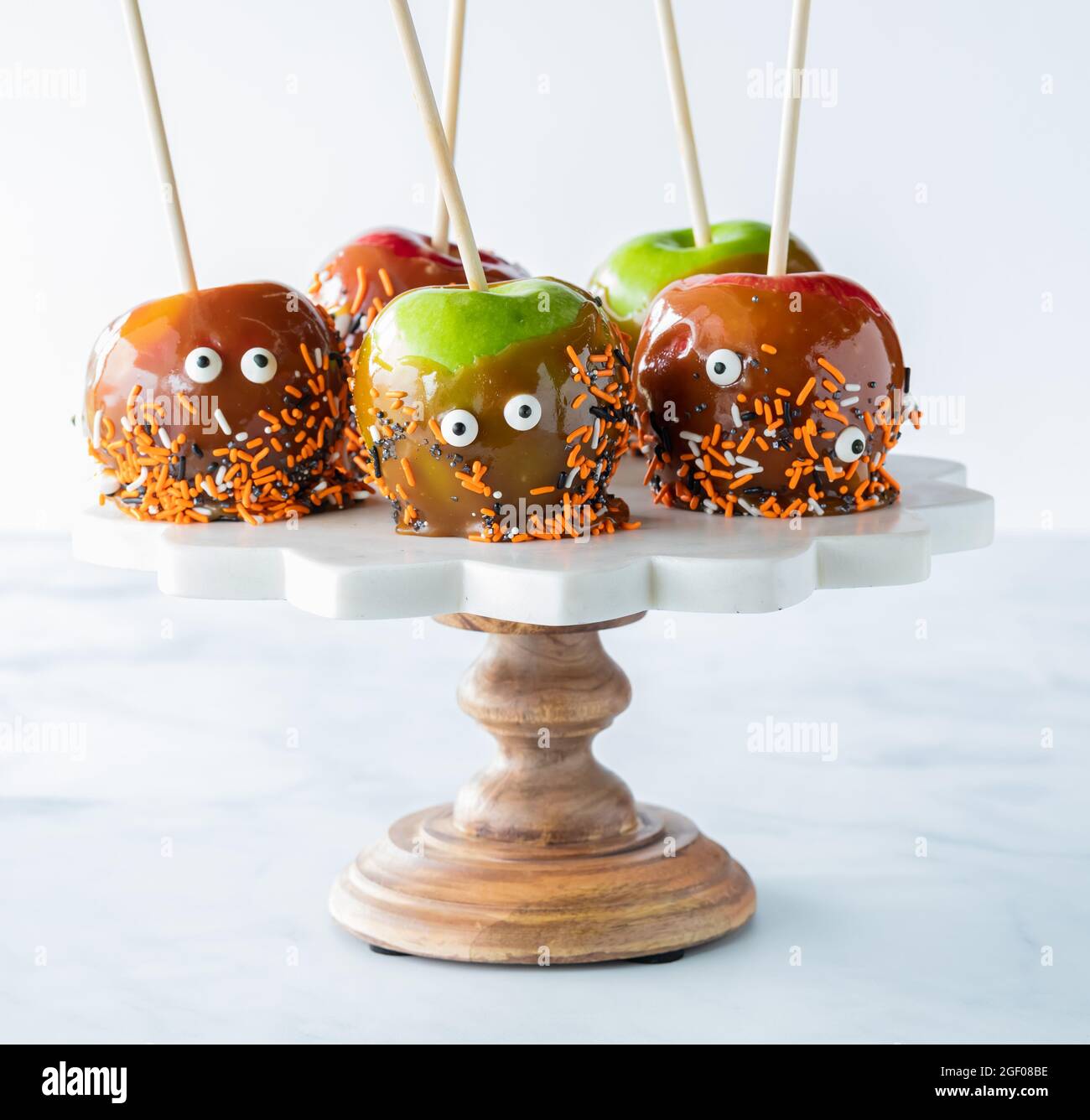 Primo piano di mele al caramello fatte in casa decorate con spolverini di Halloween su un piedistallo su uno sfondo chiaro. Foto Stock