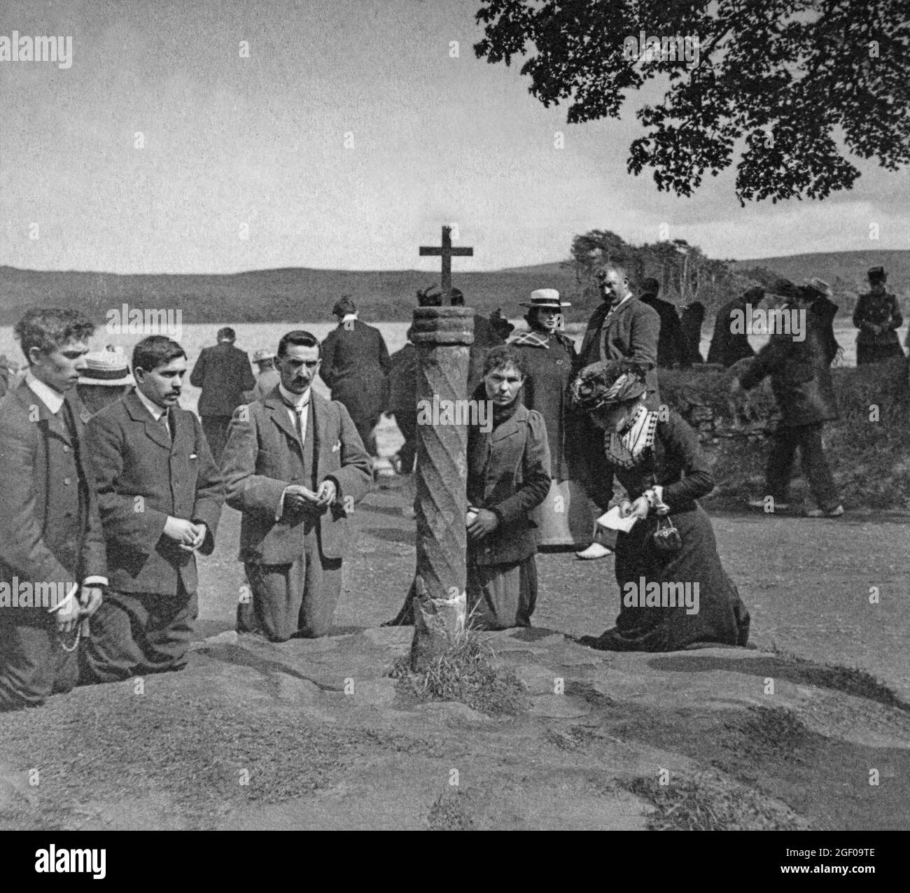 Una scena dei primi anni del XX secolo di pellegrini che pregano sul Purgatorio di San Patrizio, un luogo di pellegrinaggio sull'Isola della Stazione in Lough Derg o Loch Derg, un lago nella Contea di Donegal, Repubblica d'Irlanda. Il tradizionale pellegrinaggio di tre giorni segue un modello millenario durante il quale i partecipanti rimuovono scarpe e calzini prima di iniziare le preghiere vocali, camminando intorno all'isola, con un pasto Lough Derg ogni giorno (tè nero/caffè, toast secco, torte d'avena, acqua). Foto Stock