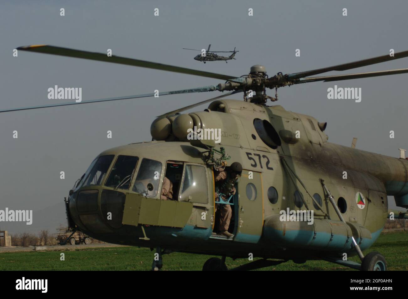 Un americano UH-60 Blackhawk si esibisce sotto controllo mentre il Crew Chief di un elicottero DELLE forze di sicurezza nazionali afghane MI-17 esegue i suoi controlli prima di prendere i comandos durante una missione di addestramento a Khanjarkhe, provincia di Parwan, Afghanistan durante una missione di addestramento. I comandos ANSF prendono parte alla loro prima missione di addestramento mentre frequentano l'Accademia di Assault dell'aria ANSF a Bagram Airfield, Afghanistan, marzo 10. Foto Stock