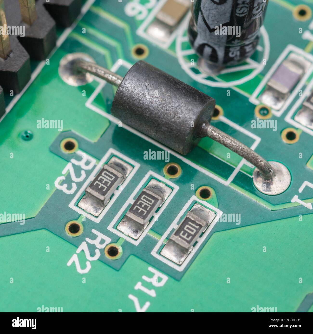 Primo piano del componente in ferrite nera a foro passante simile a un resistore sulla scheda a circuito stampato + resistori più piccoli oblunghi SM / a montaggio superficiale. Foto Stock