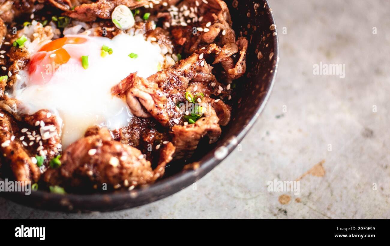 Maiale coreano con uovo sul riso in ciotola piastra di ceramica con cucchiaio di metallo e forchetta. Una tradizionale cucina coreana con piatti a base di piatti. Foto Stock