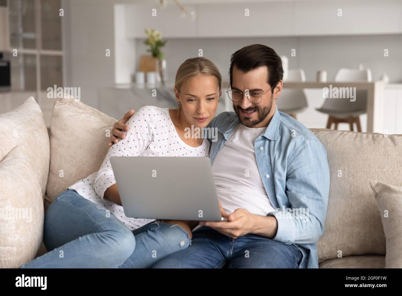 La coppia felice si è concentrata sul portatile seduto insieme sul divano Foto Stock