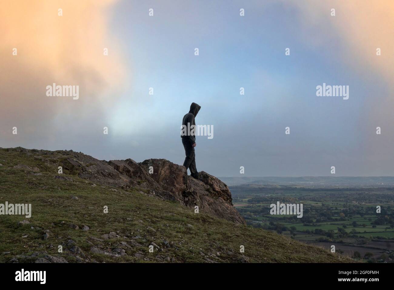 Una misteriosa figura con cappuccio. In piedi sulla cima di una collina, guardando fuori attraverso la campagna. Foto Stock