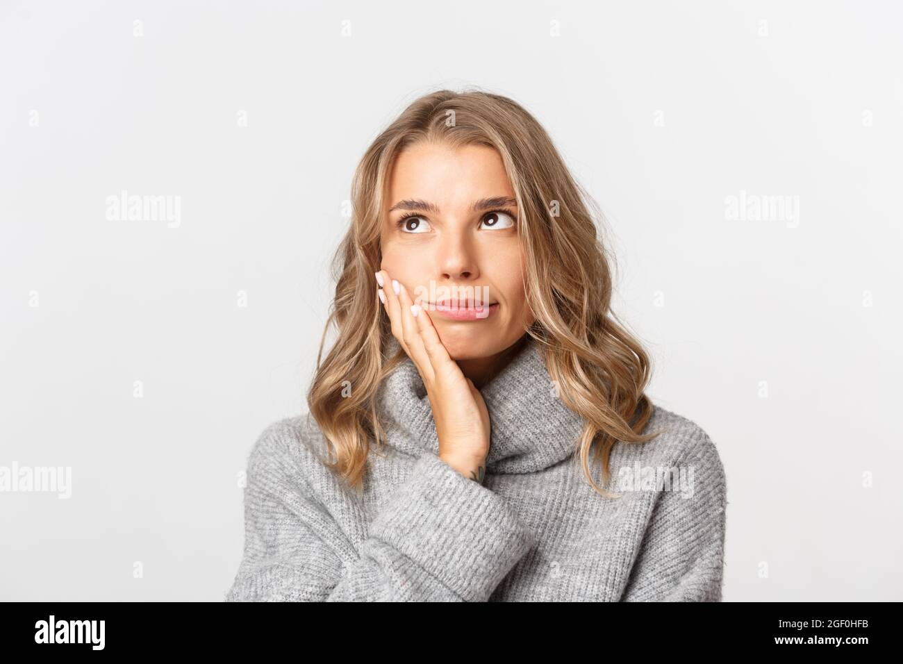 Primo piano di seccata donna bionda in pullover grigio, rotolare gli occhi e schiaffo faccia irritata con qualcosa, in piedi su sfondo bianco Foto Stock