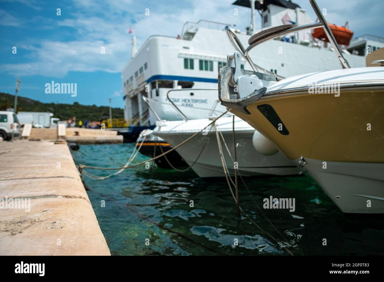 Barche arborate in un piccolo porto sull'isola di Vis, Croazia. Motoscafi su un bel mare Adriatico limpido, grande traghetto auto sullo sfondo Foto Stock