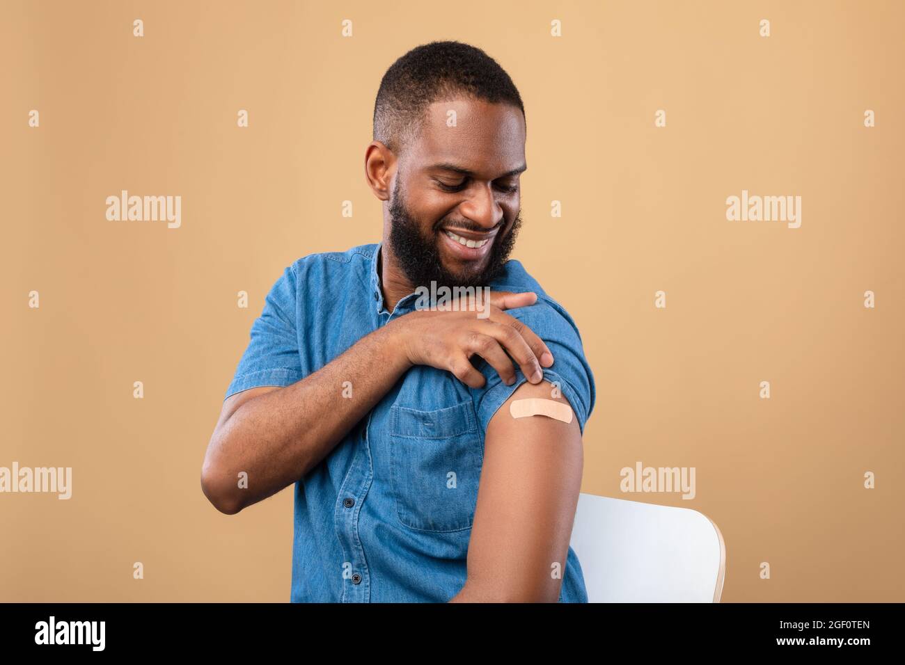 Protezione anti-covid. Uomo nero millenario che mostra braccio dopo l'iniezione di vaccino del coronavirus su sfondo beige studio Foto Stock