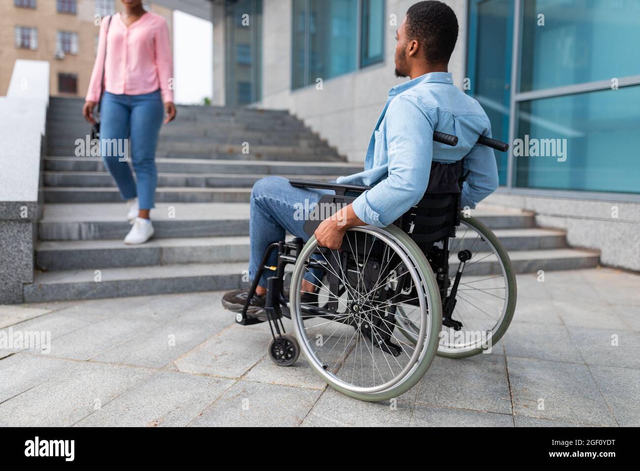Il ragazzo di colore nero per disabili che soffre di mancanza di strutture per sedie a rotelle, non può entrare nell'edificio senza rampa Foto Stock