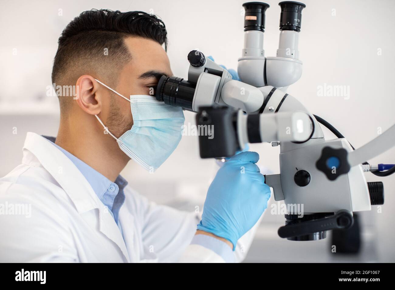 Lavoratore medico maschio arabo che usa il microscopio, facendo la ricerca nel laboratorio moderno Foto Stock