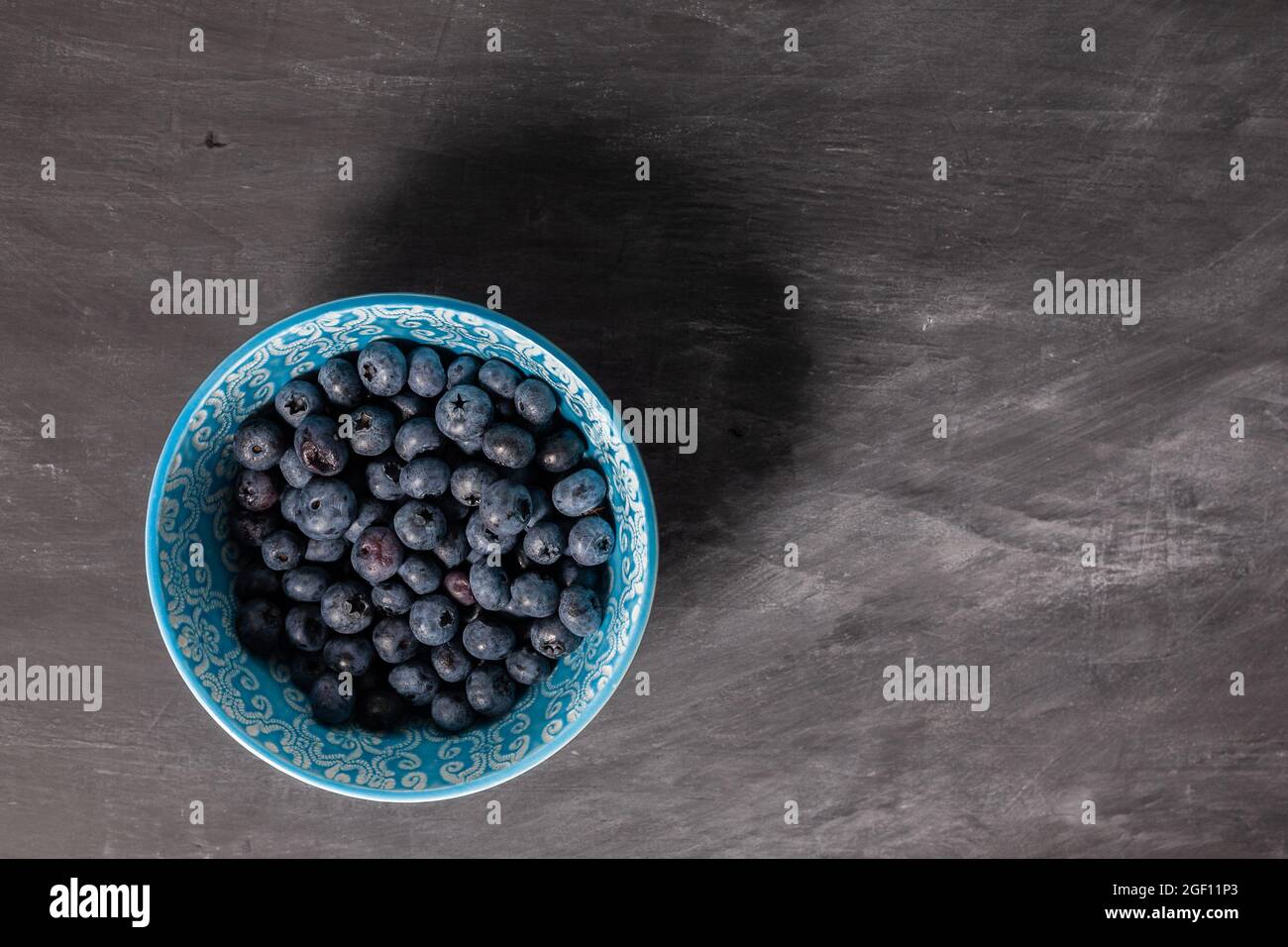 Mirtilli in ciotola blu su sfondo grigio scuro. Superficie piana. Foto Stock