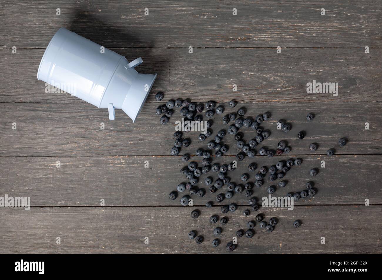 Mirtilli sparsi da una lattina su sfondo di legno grigio scuro. Foto Stock