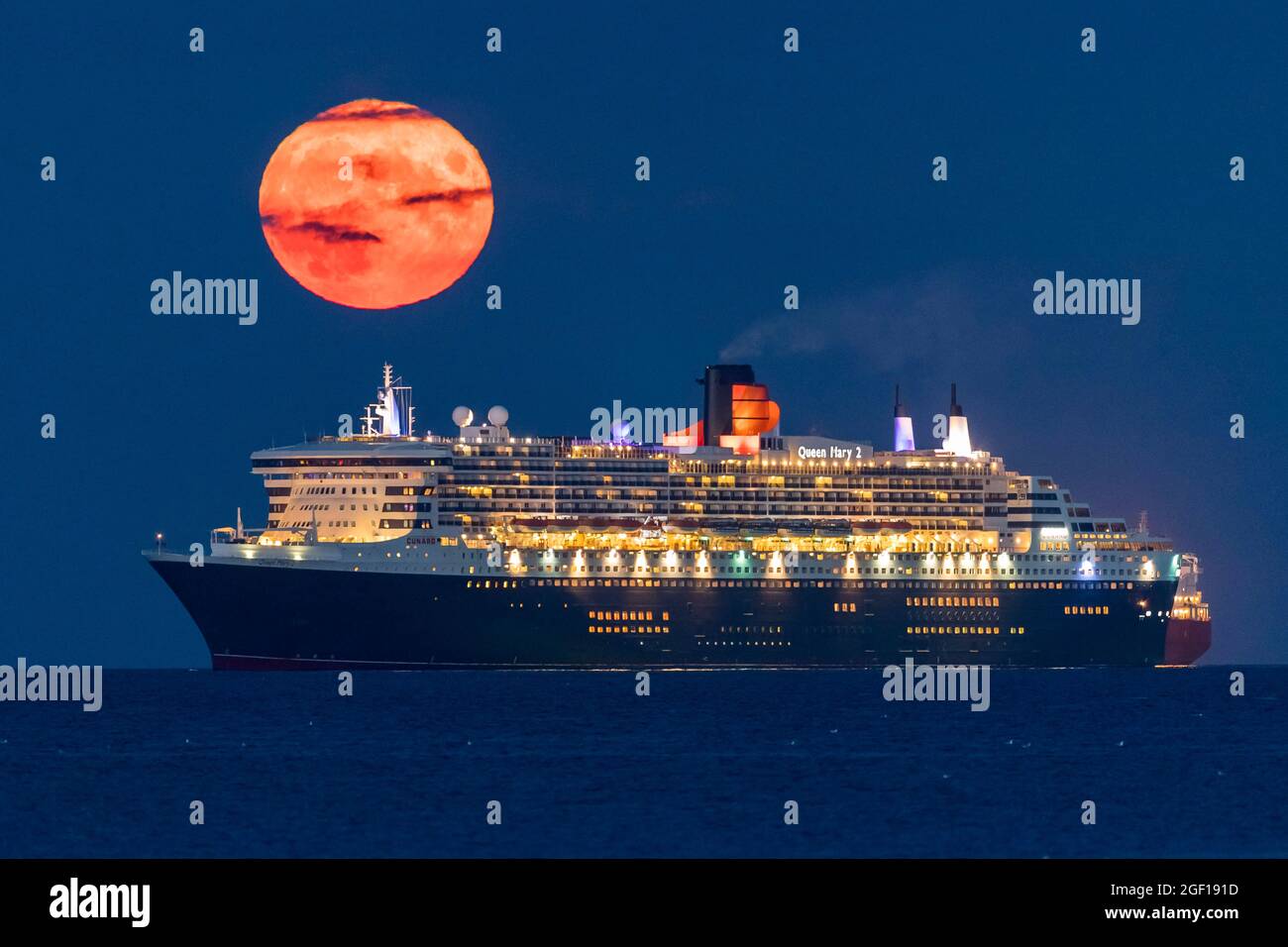 Weymouth, Dorset, Regno Unito. 22 agosto 2021. Meteo Regno Unito. La luna piena di Sturgeon si innalza verso il cielo notturno quasi limpido da dietro la nave da crociera Cunard Queen Mary 2, ancorata nella baia di Weymouth nel Dorset. Picture Credit: Graham Hunt/Alamy Live News Foto Stock