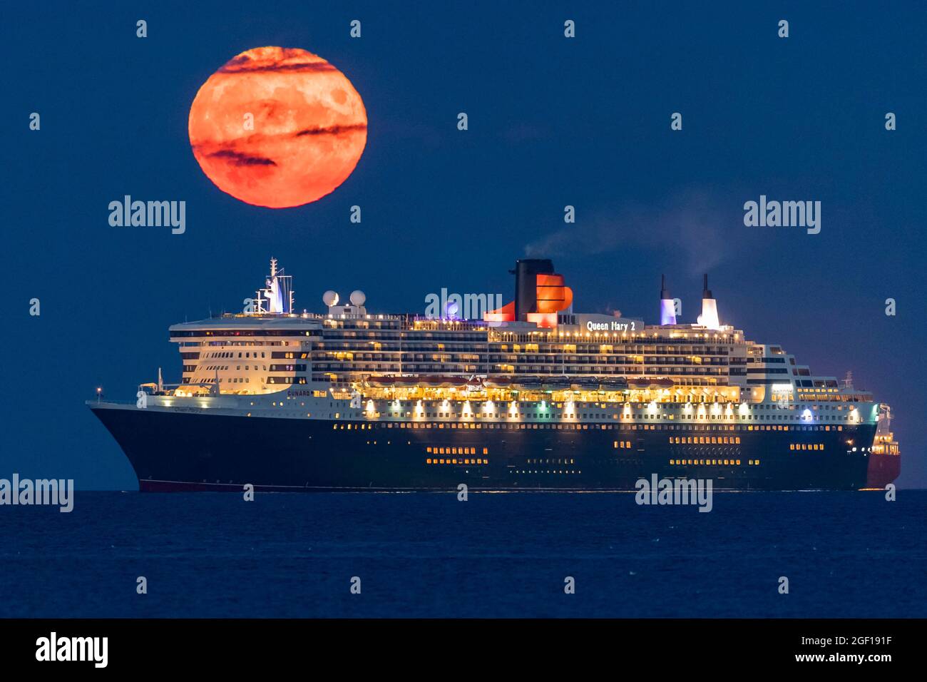 Weymouth, Dorset, Regno Unito. 22 agosto 2021. Meteo Regno Unito. La luna piena di Sturgeon si innalza verso il cielo notturno quasi limpido da dietro la nave da crociera Cunard Queen Mary 2, ancorata nella baia di Weymouth nel Dorset. Picture Credit: Graham Hunt/Alamy Live News Foto Stock