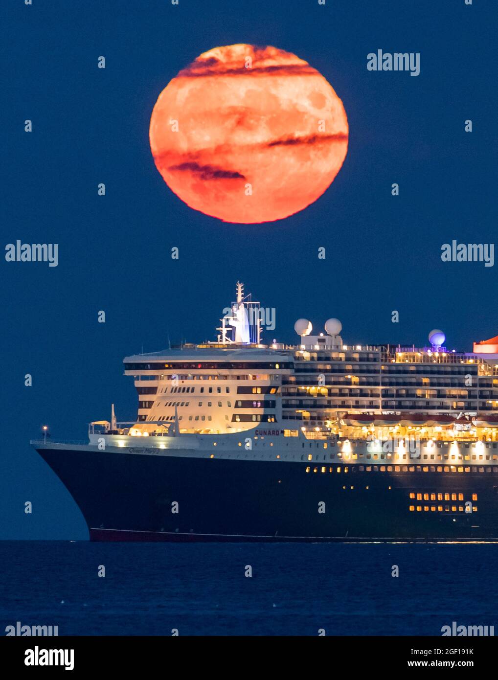 Weymouth, Dorset, Regno Unito. 22 agosto 2021. Meteo Regno Unito. La luna piena di Sturgeon si innalza verso il cielo notturno quasi limpido da dietro la nave da crociera Cunard Queen Mary 2, ancorata nella baia di Weymouth nel Dorset. Picture Credit: Graham Hunt/Alamy Live News Foto Stock