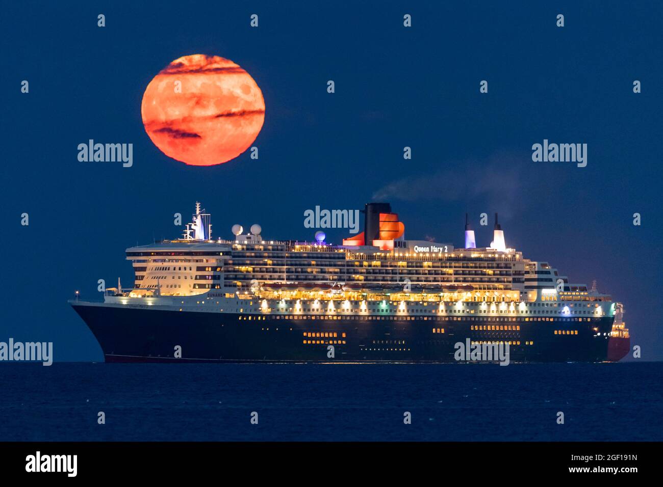 Weymouth, Dorset, Regno Unito. 22 agosto 2021. Meteo Regno Unito. La luna piena di Sturgeon si innalza verso il cielo notturno quasi limpido da dietro la nave da crociera Cunard Queen Mary 2, ancorata nella baia di Weymouth nel Dorset. Picture Credit: Graham Hunt/Alamy Live News Foto Stock
