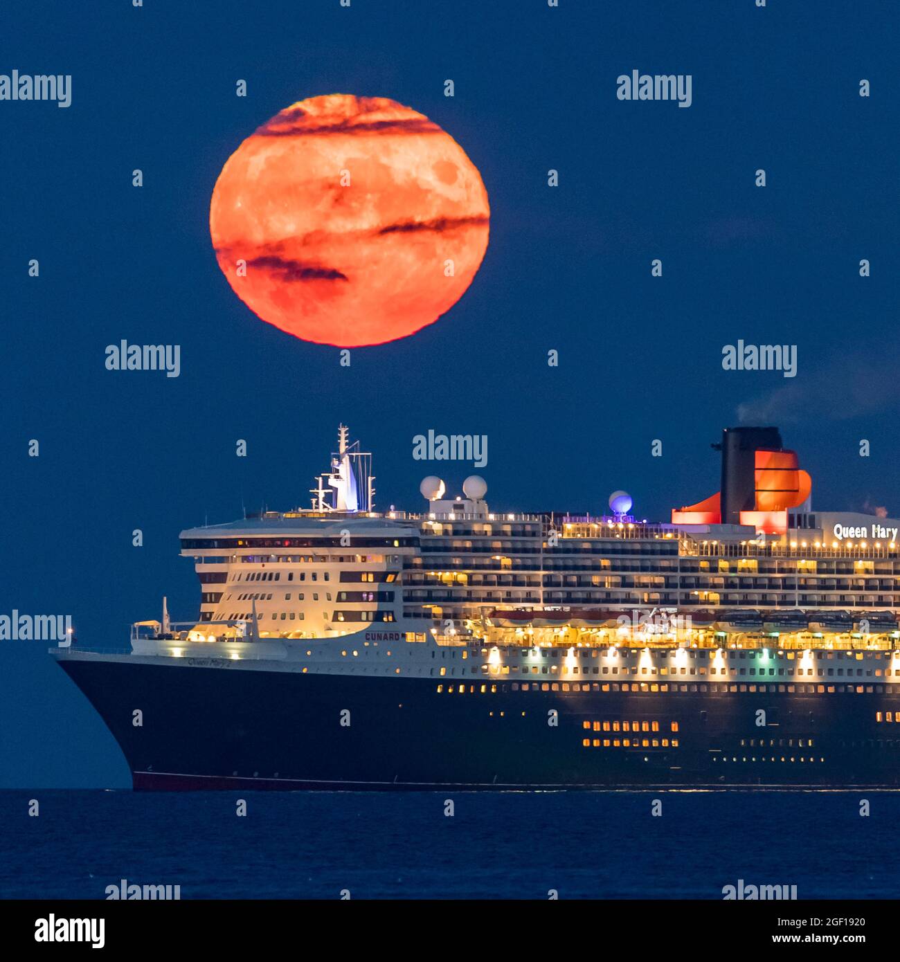 Weymouth, Dorset, Regno Unito. 22 agosto 2021. Meteo Regno Unito. La luna piena di Sturgeon si innalza verso il cielo notturno quasi limpido da dietro la nave da crociera Cunard Queen Mary 2, ancorata nella baia di Weymouth nel Dorset. Picture Credit: Graham Hunt/Alamy Live News Foto Stock