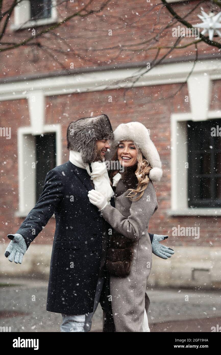 Felice coppia amorevole godere a piedi all'aperto nella neve caduta in città durante le vacanze invernali a Natale Foto Stock