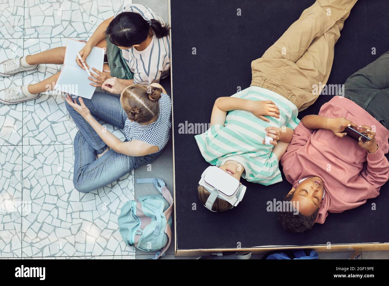 Vista dall'alto in basso in un gruppo di bambini che si rilassano e utilizzano la realtà virtuale durante la pausa alla scuola moderna Foto Stock