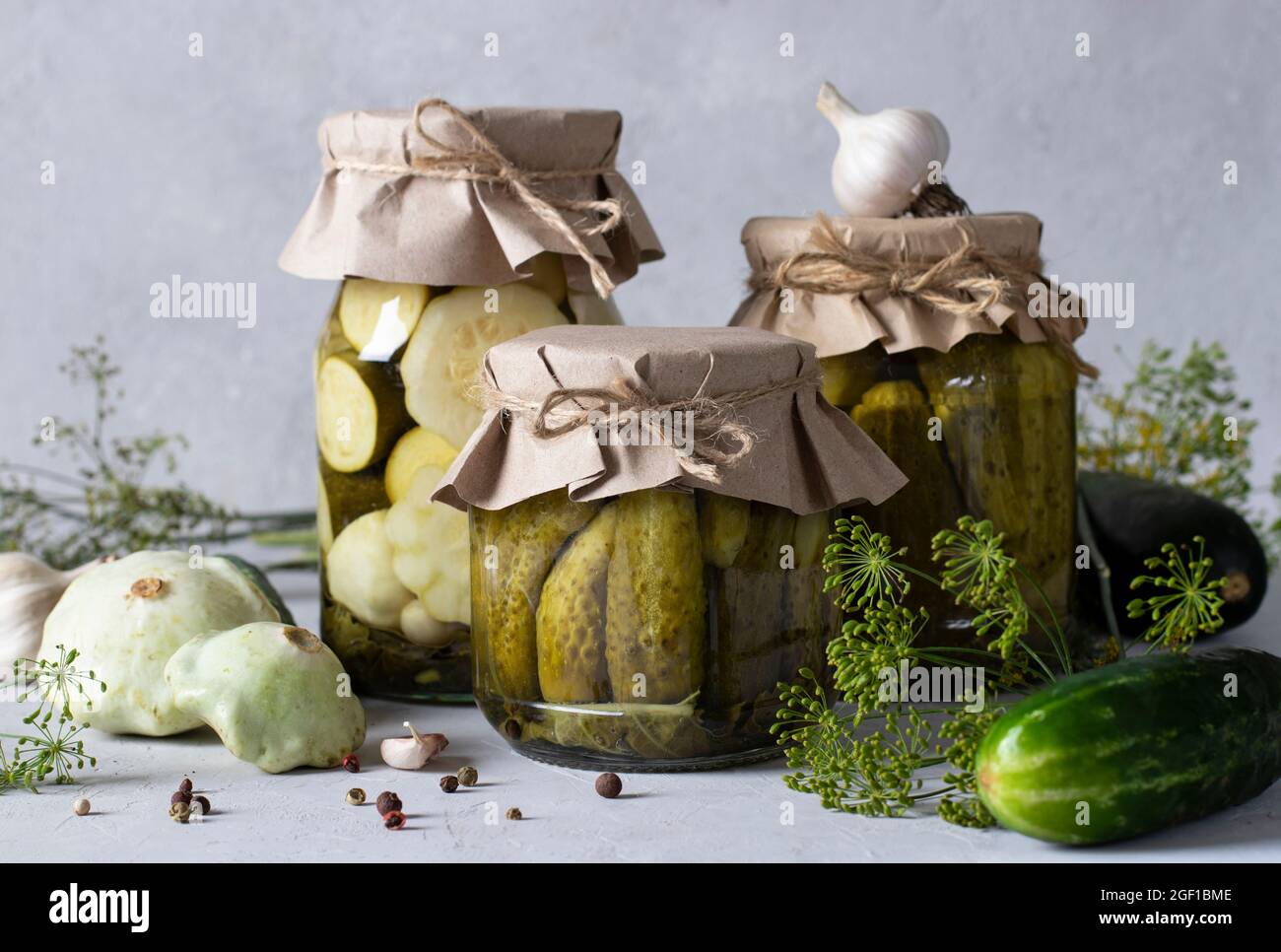 Cetrioli sottaceto fatti in casa, patissons e zucchine in vasetti di vetro su sfondo grigio chiaro con ingredienti freschi, Closeup. Foto Stock