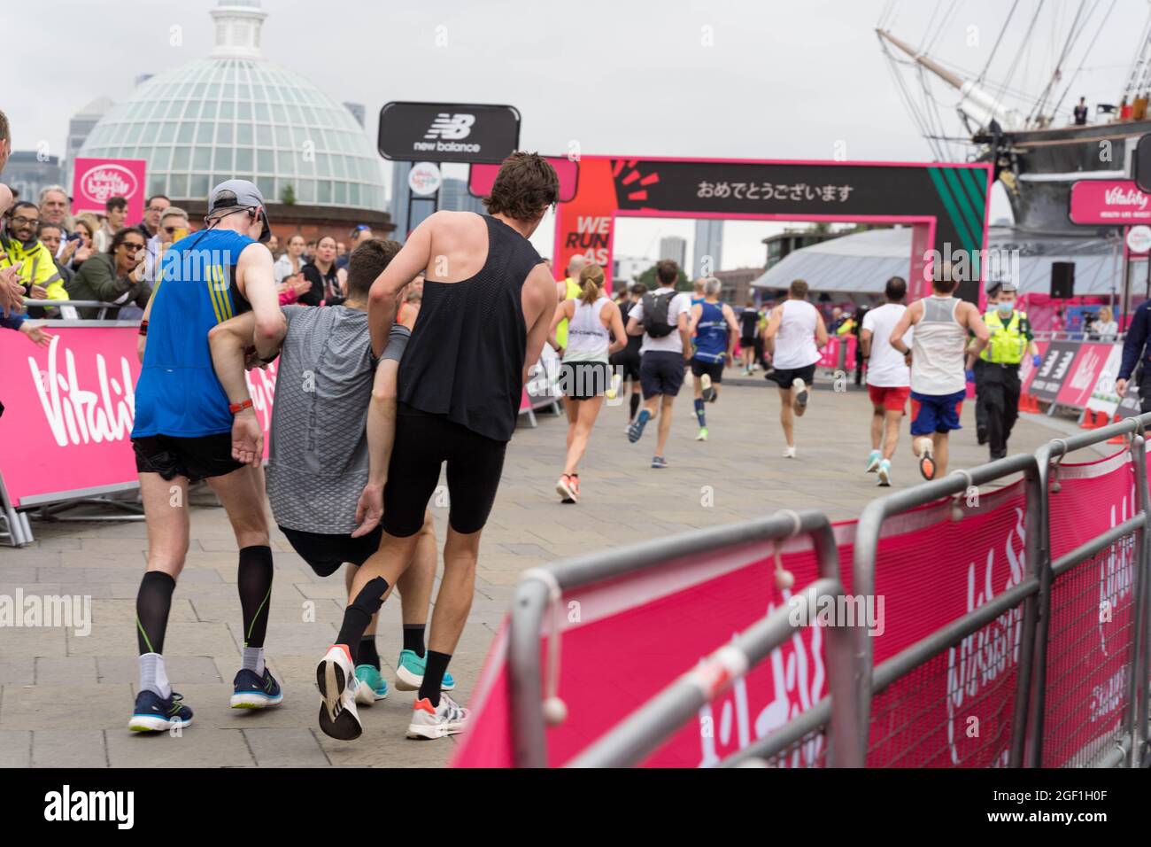 Due corridori aiutano un uomo con gamba schiacciata al traguardo a mezza maratona al Cutty Sark London Greenwich UK, grande mezza maratona Foto Stock
