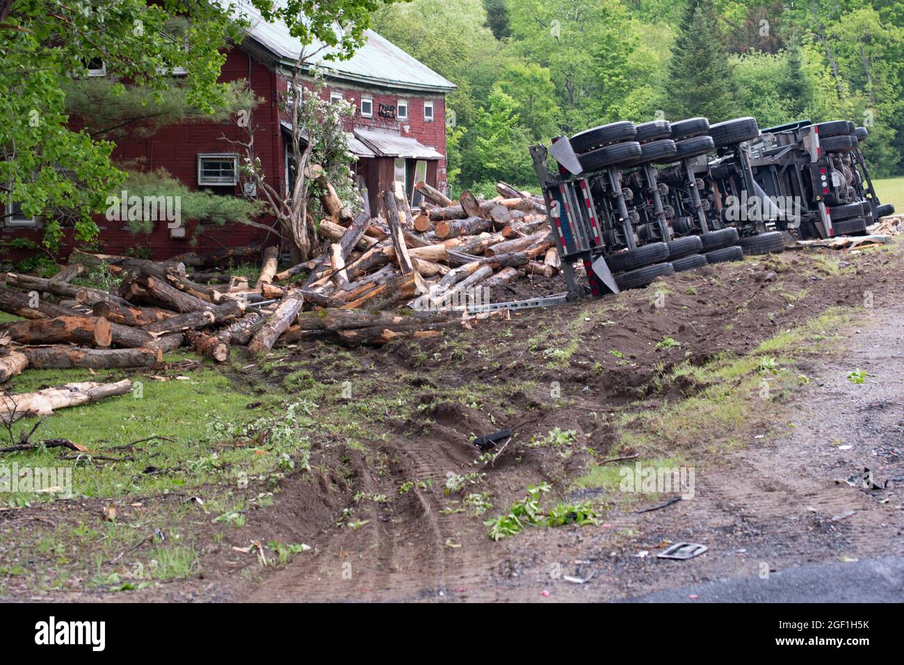 Un incidente di camion di trasporto del ceppo in Hoffmeister, NY USA che coinvolge un camion di taglio rotolare sul suo lato e scaricare un carico di tronchi sulla parte anteriore di una casa. Foto Stock