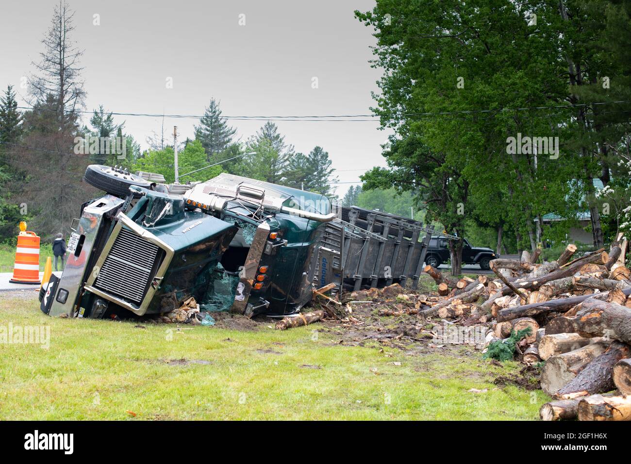 Un incidente di camion di trasporto del ceppo in Hoffmeister, NY USA che coinvolge un camion di taglio rotolare sul suo lato e scaricare un carico di tronchi sulla parte anteriore di una casa. Foto Stock