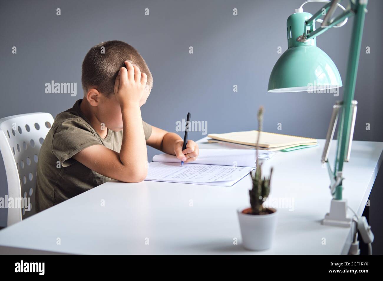 Lo scolaro seduto al tavolo e facendo il lavoro scolastico a casa. Concetto di homeschooling. Foto Stock