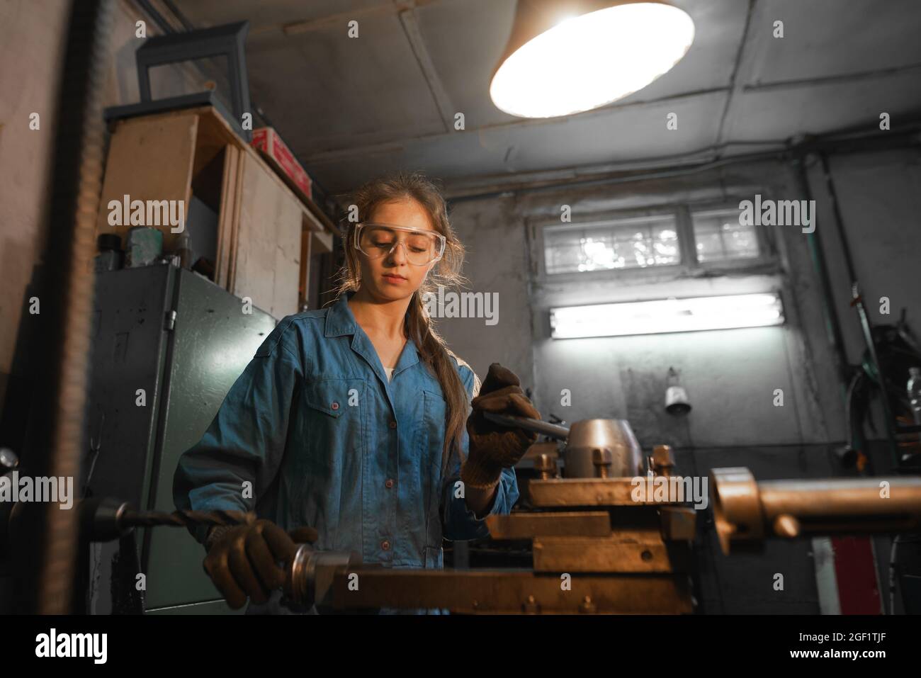la giovane donna nel suo garage lavora su un tornio. Professione concetto Turner, lavorazione dei metalli, tornitura, industria, metallo. Foto Stock
